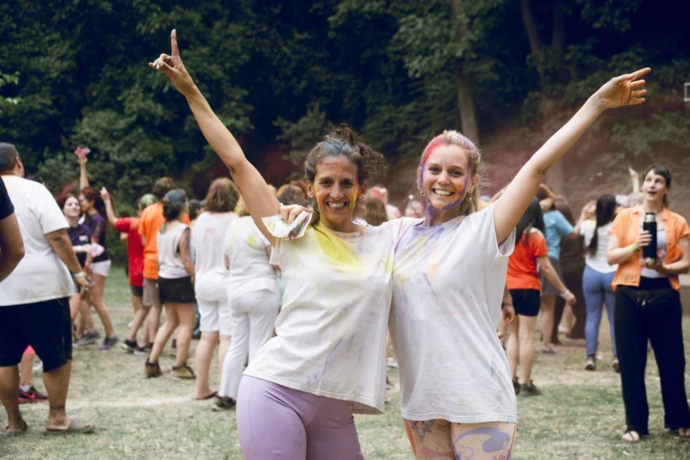 Dos participantes abrazadas y cubiertas de colores en Holi 2024