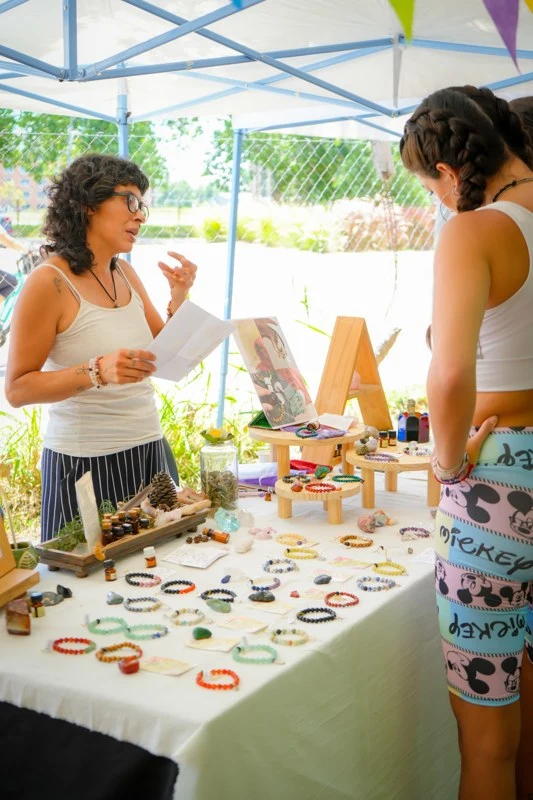 Artesana compartiendo sus productos con una visitante en Holi 2025