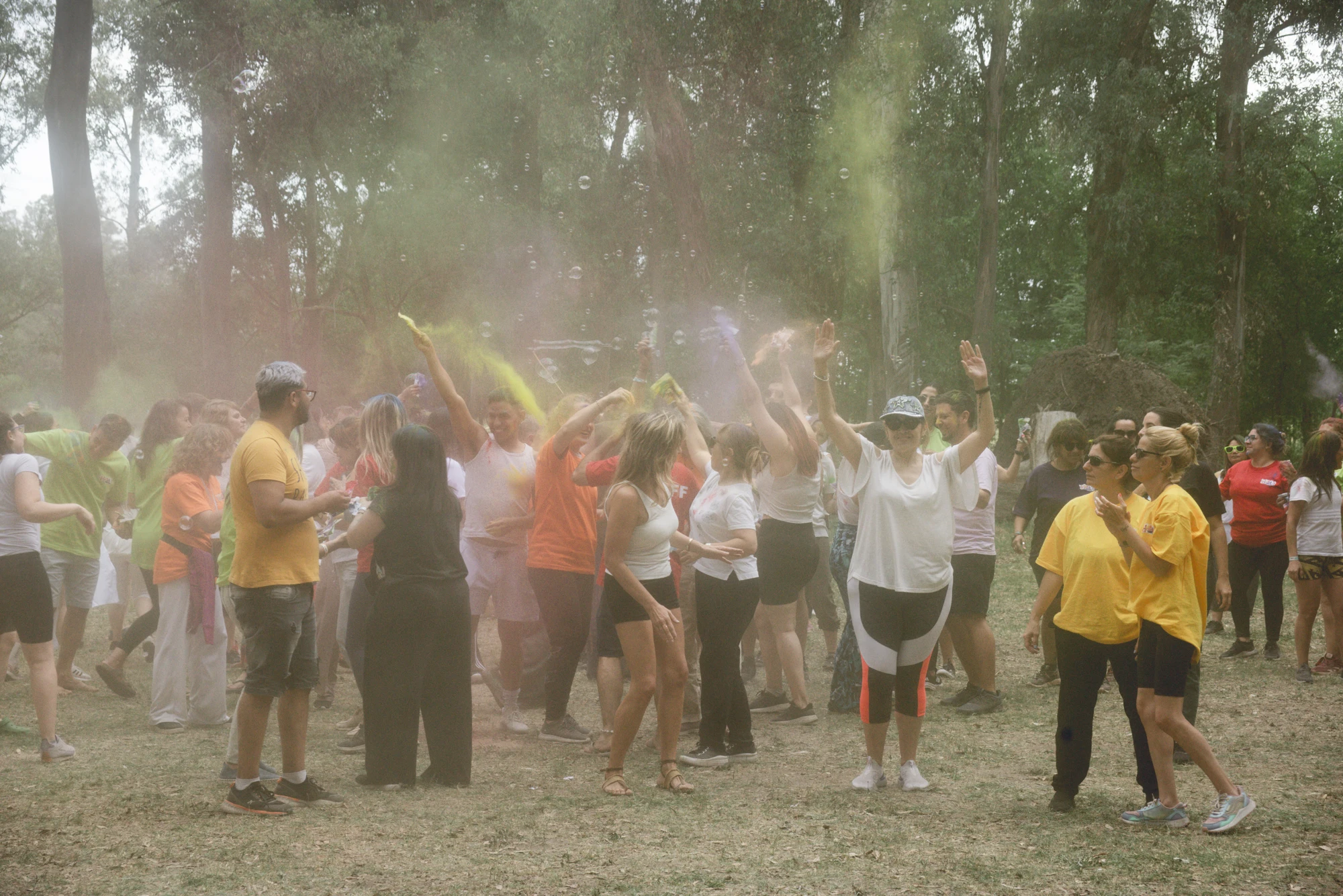 Participantes celebrando con polvos de colores entre árboles en Holi 2024
